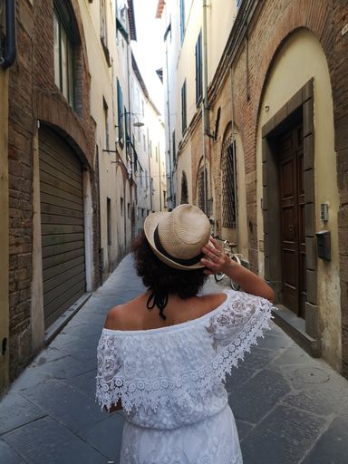A vertical shot of a tourist woman with a white dress and straw summer hat in an alley in Lucca, Italy