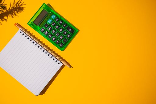 A top view of a vibrant orange surface with a green calculator on it next to a notebook with a pencil