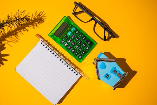 A top view of a bright orange surface with stationery pieces on it next to a pair of glasses and a toy
