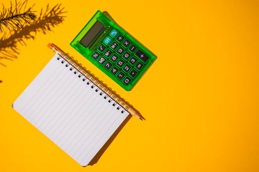 A top view of a bright orange surface with a calculator and notebook on it next to a small branch