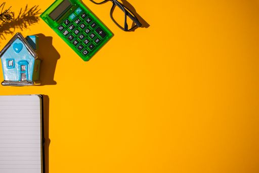 A top view of an orange background with stationery pieces and glasses on it with shadows under them
