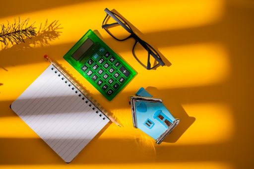 A top view of a vibrant orange shadowy surface with stationery objects on it next to a pair of glasses