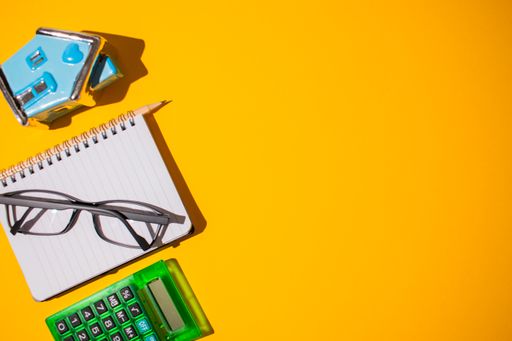 A top view of a vibrant orange shadowy surface with stationery on it next to a small blue house toy