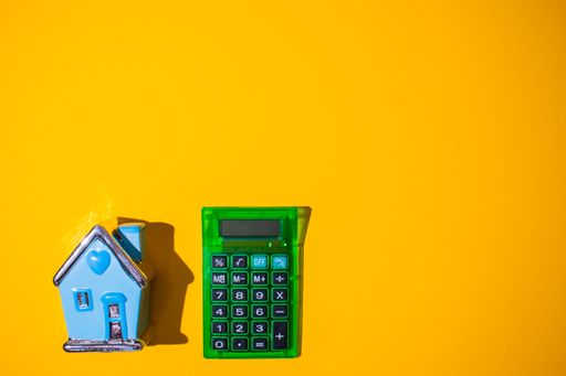 A top view of a bright orange surface with a small house toy and a green calculator on it