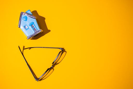 A top view of a bright orange surface with a small house toy on it next to a pair of glasses