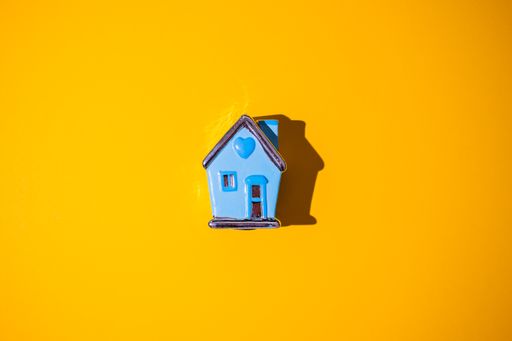 A top view of a neon orange surface with a small ceramic house toy on it in the middle