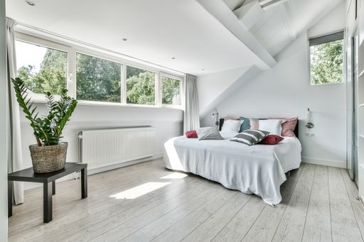 A modern bedroom in white colors with a large bed and windows