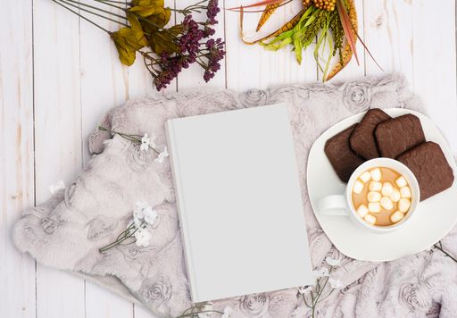 An overhead shot of a white book next to a sweet drink with chocolate cookies on a plate