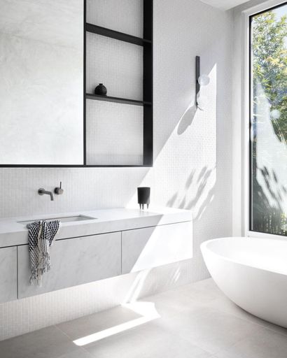 A vertical shot of an elegant white modern bathroom with a simple round tub and minimalistic cabinets