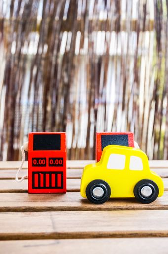 A vertical shot of a wooden yellow toy car in front of two red wooden gas pump toys