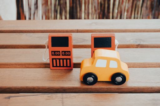A wooden yellow toy car in front of two red wooden gas pump toys