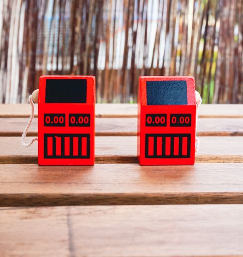 A vertical shot of two red wooden gas pump toys on a wooden table