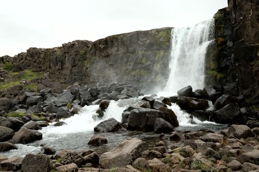 A scenic waterfall cascades over rocky terrain, surrounded by lush greenery and a cloudy sky, capturing the essence of nature's beauty.