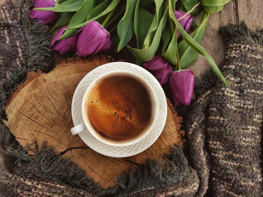 A high angle shot of a cup of coffee and some tulip flowers on a wooden surface