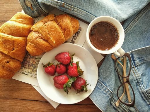 A high angle shot of a cup of coffee, croissants, and a plate of strawberries