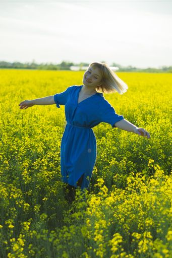 A beautiful female in a blue dress dancing happily in a yellow flower field