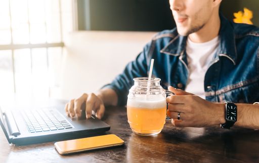A young man working on a laptop and holding a pint of beer