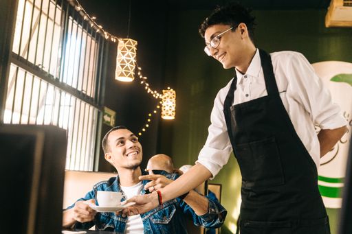 A cheerful waiter in serving a cup of coffee to a young happy Hispanic customer