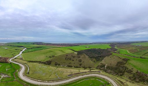 Aerial view of the lush green South Downs landscape with winding river under a cloudy sky, showcasing the beauty of the English countryside.