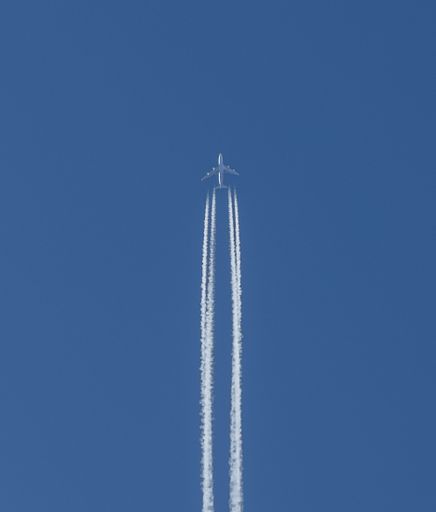 Airplane flying high in the clear blue sky leaving contrails behind, symbolizing travel and aviation.