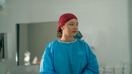 A young female healthcare worker in scrubs and red headscarf in a hospital setting.