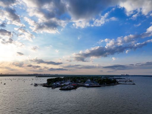 Aerial view of a serene island surrounded by calm waters under a partly cloudy sky during sunset.