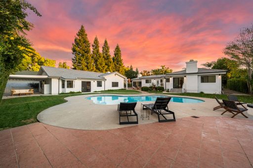 A luxurious modern house with a pool and patio at sunset, surrounded by lush greenery and a vibrant sky.