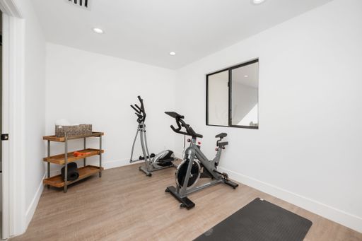 Modern home gym with exercise bikes, yoga mat, and storage shelves in a bright, minimalist room.