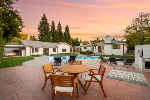 Beautiful backyard with pool, patio furniture, and sunset sky, surrounded by trees and a modern house.
