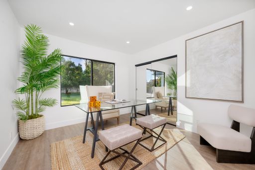 Modern home office with glass desk, stylish chairs, and large window view of garden, featuring minimalist decor and natural light.