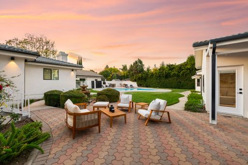 Elegant backyard patio with modern furniture, a pool, and lush greenery at sunset, creating a serene outdoor retreat.
