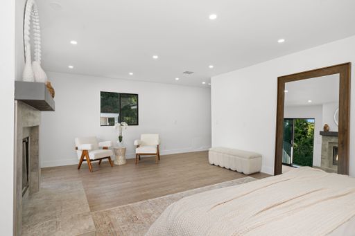 Modern minimalist bedroom with white walls, wooden floor, and elegant furniture, featuring a large mirror and natural light.