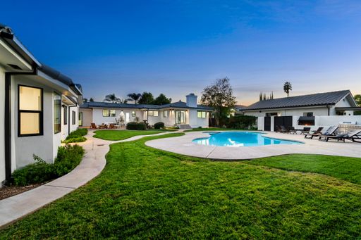 Modern backyard with a swimming pool, green lawn, and patio furniture under a clear evening sky.