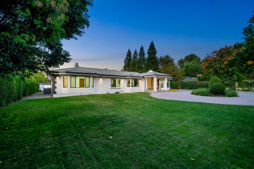 Modern single-story home surrounded by lush greenery and a clear evening sky, showcasing a manicured lawn and contemporary architecture.