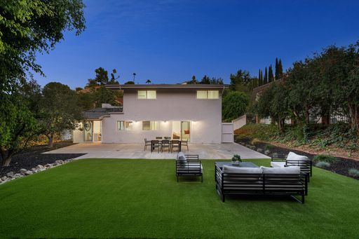 Modern house with spacious backyard, outdoor seating, and lush greenery in a suburban setting during twilight.