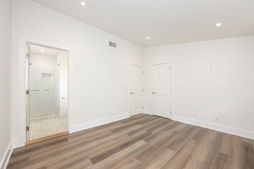 Bright, empty room with wooden flooring and a modern bathroom, featuring white walls and recessed lighting.