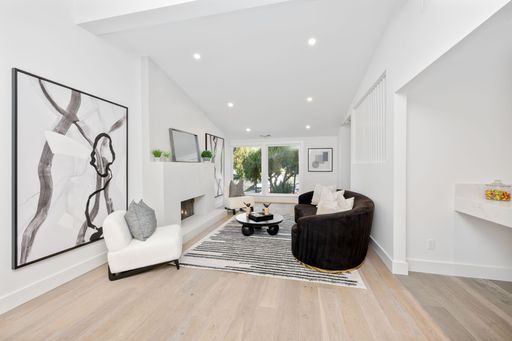 Modern living room with abstract art, black sofa, and large windows offering natural light, featuring a cozy fireplace.