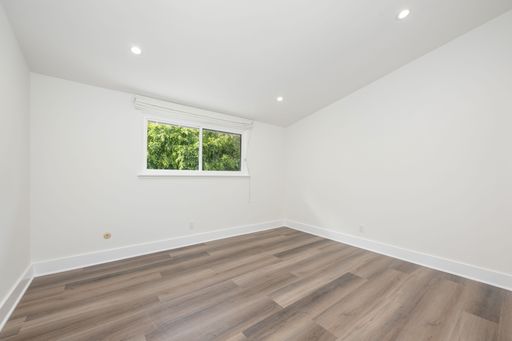 Modern empty room with wooden flooring and a large window showing greenery outside, ideal for real estate or interior design concepts.