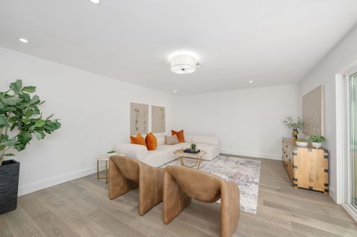 Modern living room interior with white walls, wooden flooring, and stylish furniture including a beige sofa and brown chairs.