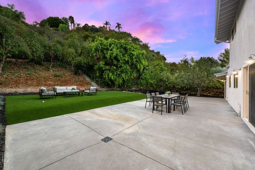 Spacious backyard patio with modern furniture, lush greenery, and a vibrant sunset sky.