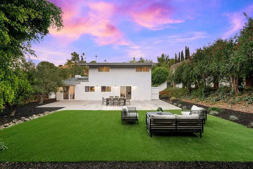 Modern backyard with lush green lawn, outdoor seating, and vibrant sunset sky in suburban setting.