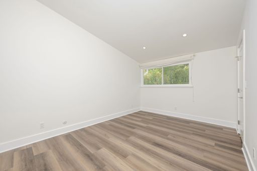 Empty modern room with white walls and wooden flooring, featuring a large window with a view of greenery, creating a bright and airy space.
