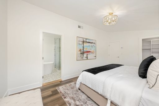 Modern bedroom interior with elegant decor, featuring a cozy bed, abstract art, and an en-suite bathroom with a bathtub.