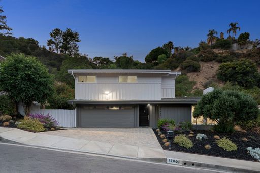 Modern suburban house exterior at twilight with landscaped front yard, surrounded by lush hills and trees.
