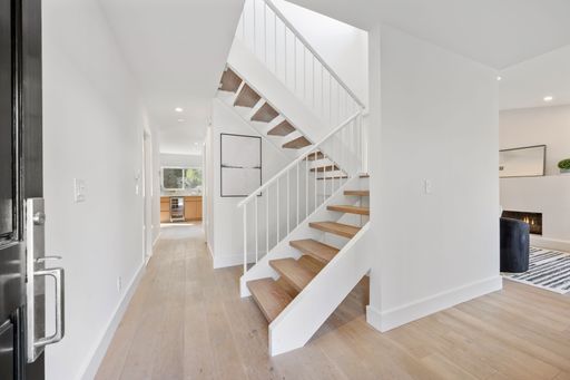 Modern interior hallway with wooden flooring and a white staircase leading to the upper floor, bright and minimalist design.
