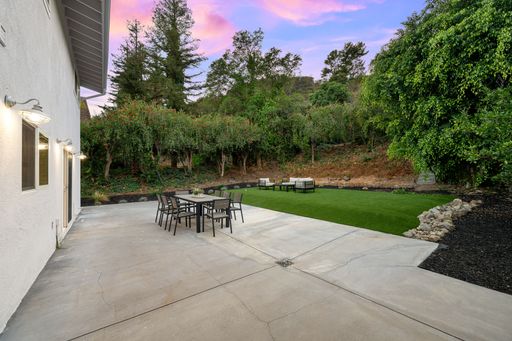 Modern backyard patio with outdoor furniture and lush greenery under a vibrant sunset sky.