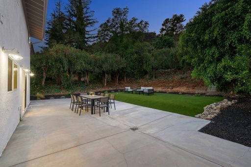 Modern backyard patio with outdoor dining set and lush greenery at dusk.