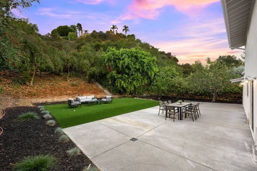 A modern backyard patio with outdoor furniture, lush greenery, and a vibrant sunset sky.
