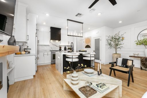 Modern kitchen interior with sleek white cabinetry, marble countertops, and stylish decor, featuring a wooden floor and contemporary lighting.