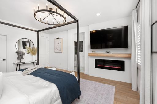 Modern bedroom interior with a canopy bed, wall-mounted TV, and electric fireplace, showcasing minimalist decor and neutral tones.